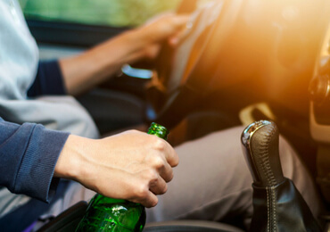 a drunk driver holding an alcoholic drink wile driving